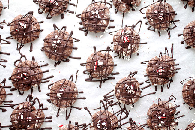 Overhead view of chocolate thumbprint cookies drizzled with chocolate on a piece of white parchment paper.