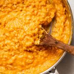 Wooden spoon stirring butternut squash puree into risotto.