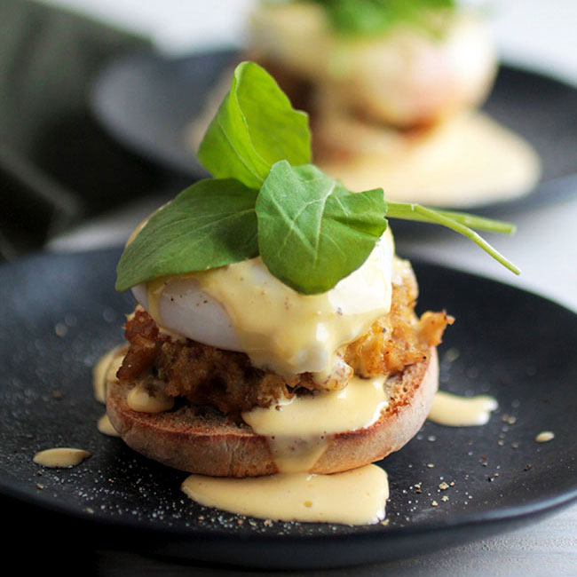 Crabcake eggs benedict on a navy plate, topped with fresh arugula.