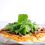 Small pizza topped with fresh arugula on a white table.