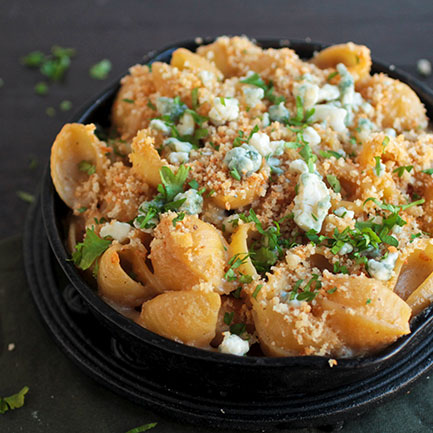 A small cast iron skillet filled with shell pasta, topped with blue cheese and fresh parsley.