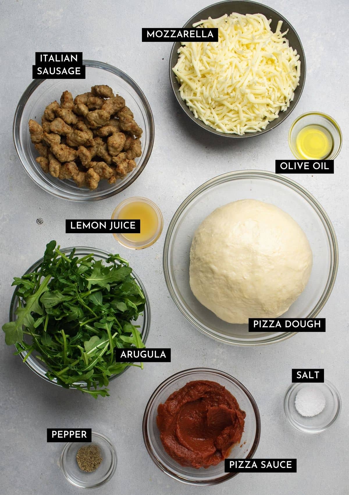 Pizza ingredients, organized into individual bowls on a white table.
