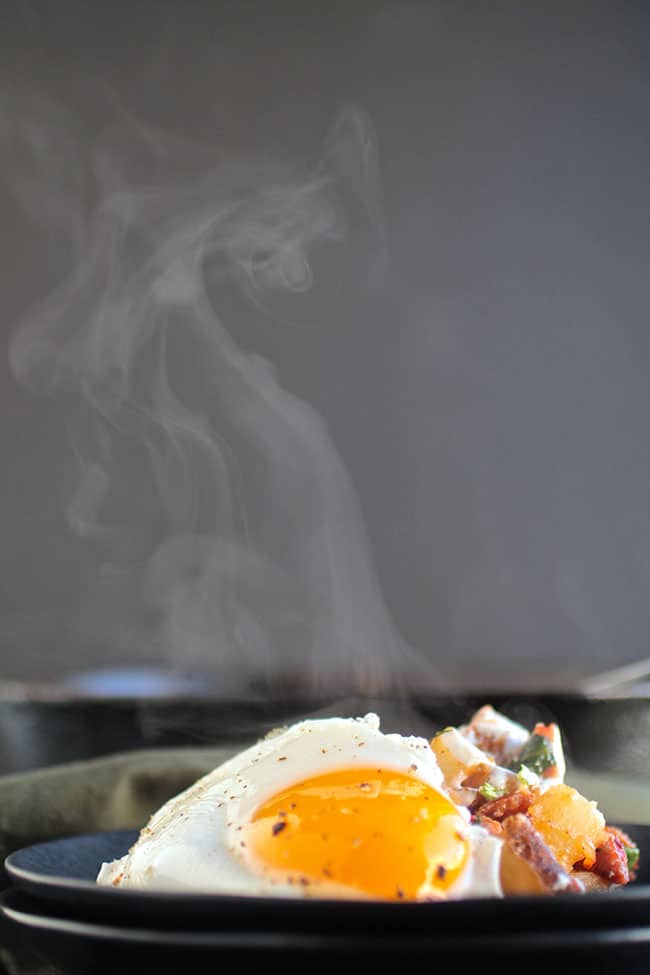 A dark plate with hash, topped with a steaming hot fried egg.
