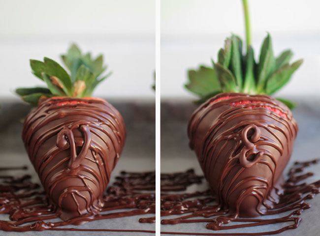 Two chocolate covered strawberries sitting on a piece of parchment paper with melted chocolate drizzled on top.
