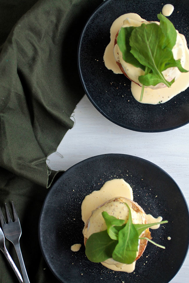 Aerial view of two navy blue plates with crab cake eggs benedict next to a dark green napkin.