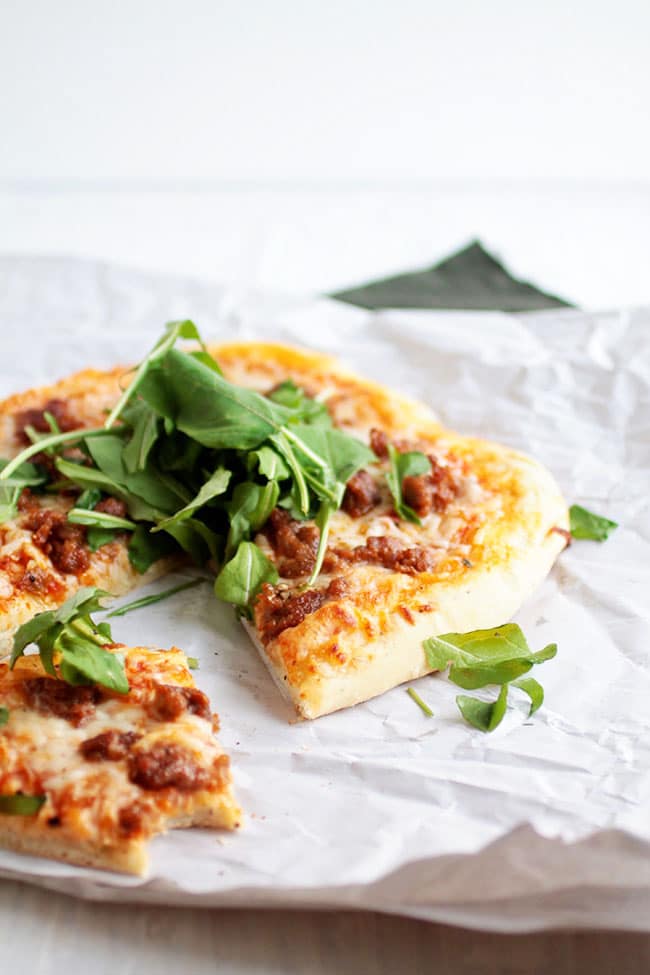 Small pizza topped with fresh arugula, with one slice removed.