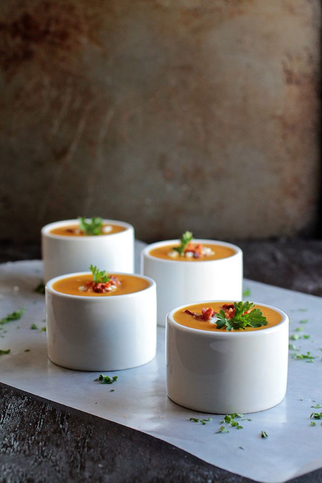 Four small white bowls filled with butternut squash soup.