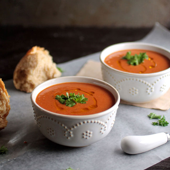 Two white bowls filled with red pepper soup.