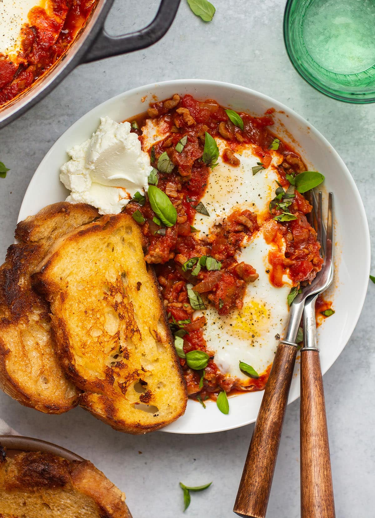 Baked eggs in a shallow white bowl with sourdough toast and whipped goat cheese.