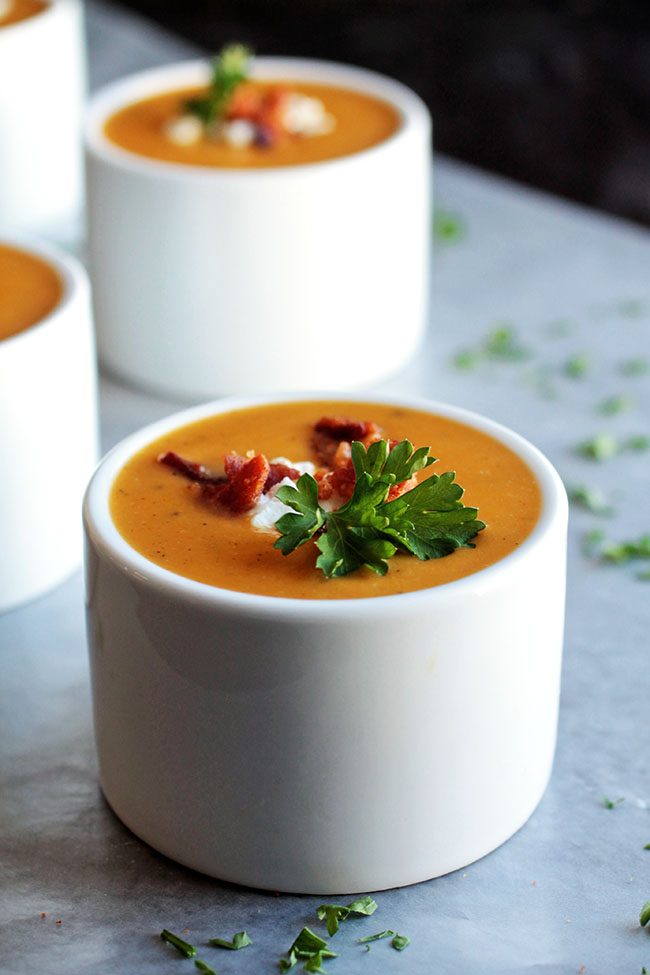 Bright orange butternut squash soup in a white bowl, topped with fresh parsley.