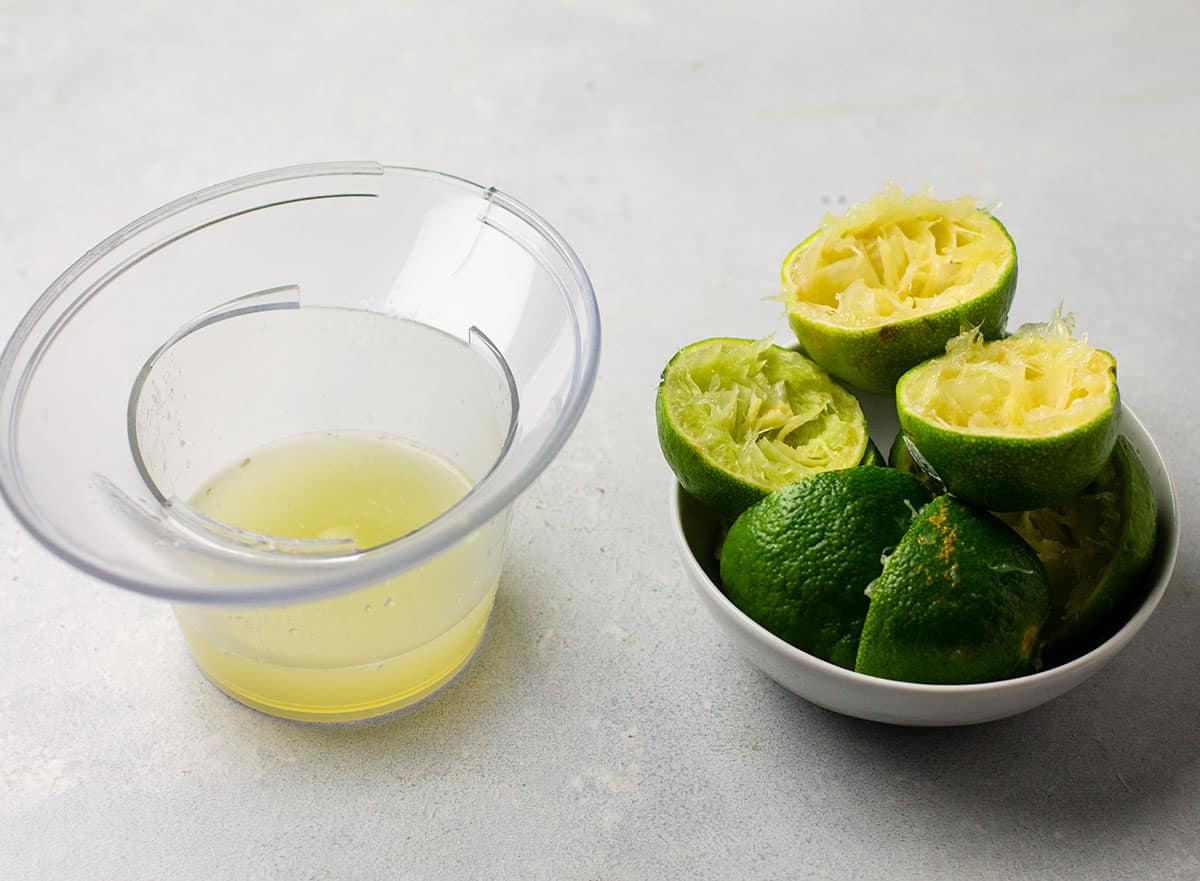 Lime juice in a plastic cup, next to a pile of limes.