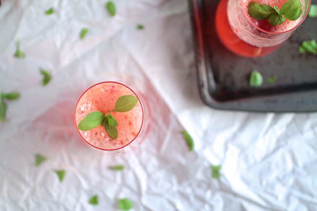 Close up of a sprig of fresh basil inside a champagne glass filled with pink bourbon spritzer.