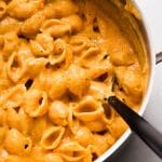 Black spoon stirring shell pasta with butternut squash sauce in a large pot.