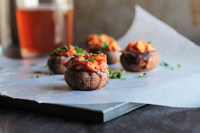 Stuffed mushrooms on a slate serving platter in front of a glass of beer.
