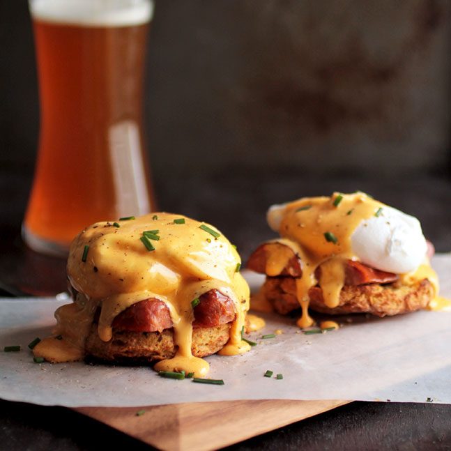 Eggs benedict on a wood serving board in front of a dark background.