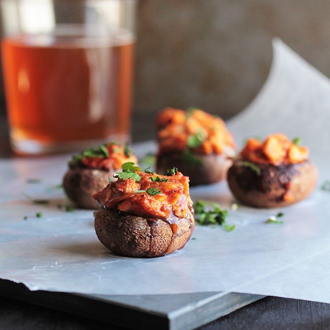 Stuffed mushrooms on a dark table in front of a glass of beer.