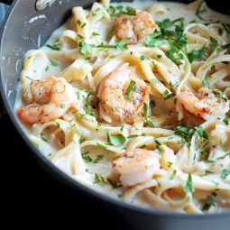 Alfredo topped with cooked shrimp and fresh parsley, in a dark pot.