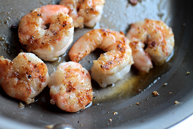 Cooked shrimp in a dark skillet.