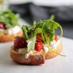 Toast topped with burrata cheese, tomatoes, and fresh arugula on a white table.