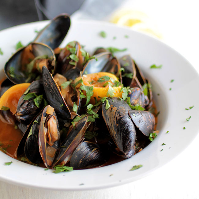 Mussels, lemon wedges, and chipotle sauce in a shallow white bowl.