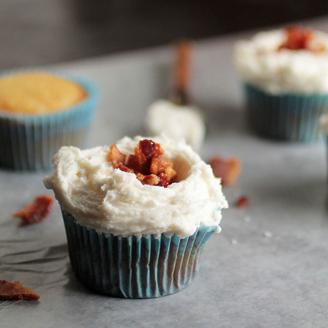 Vanilla cupcake topped with frosting and bacon pieces.