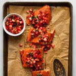 Salmon fillet topped with strawberry salsa on a baking sheet lined with brown parchment paper.