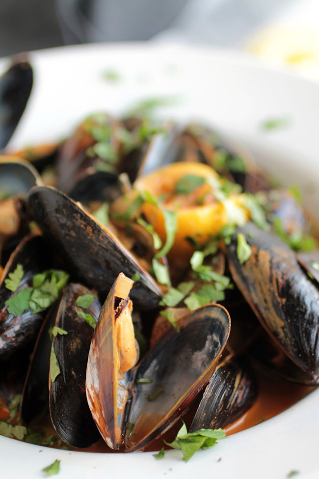 Close up of cooked, opened mussels topped with fresh chopped cilantro.