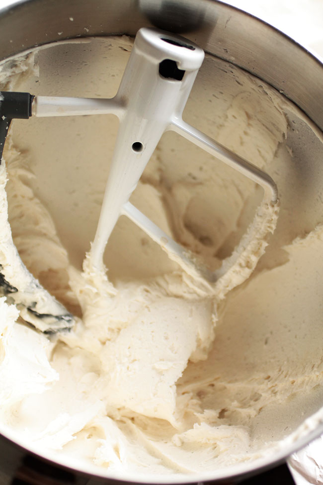 White paddle mixing vanilla frosting in the bowl of a stand mixer.