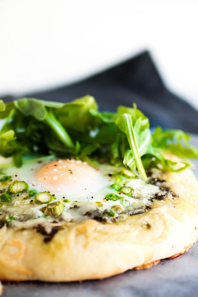 Close up of a baked egg on top of a breakfast pizza, topped with fresh arugula.