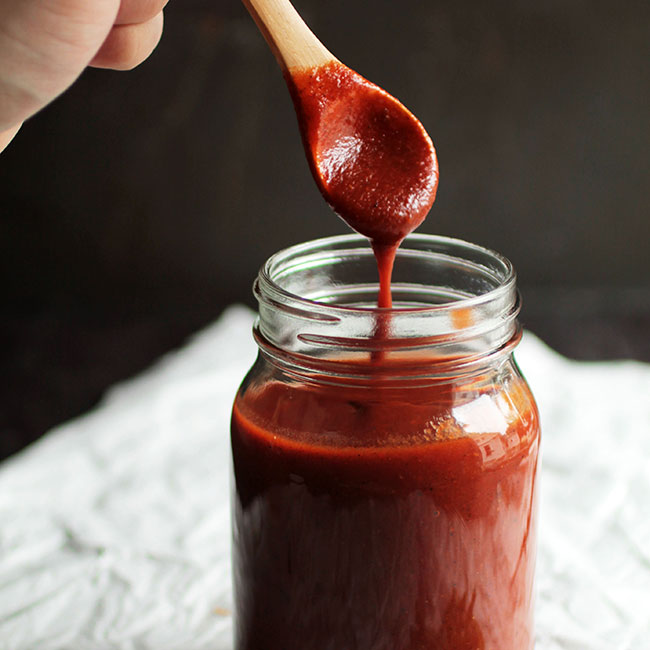 Wooden spoon being dipped in a mason jar full of enchilada sauce.