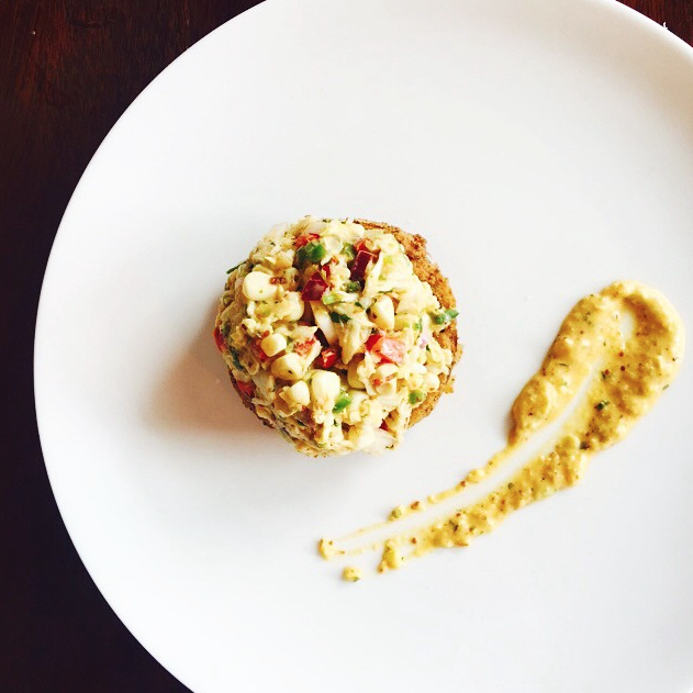 Crab cake topped with corn salsa on a white plate.