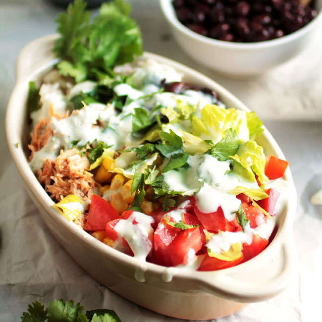 Burrito bowl drizzled with sour cream in a tan serving dish.