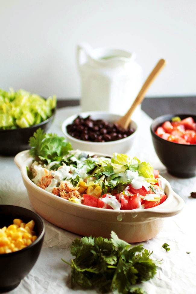 A burrito bowl surrounded by small bowls of ingredients on a brown table.