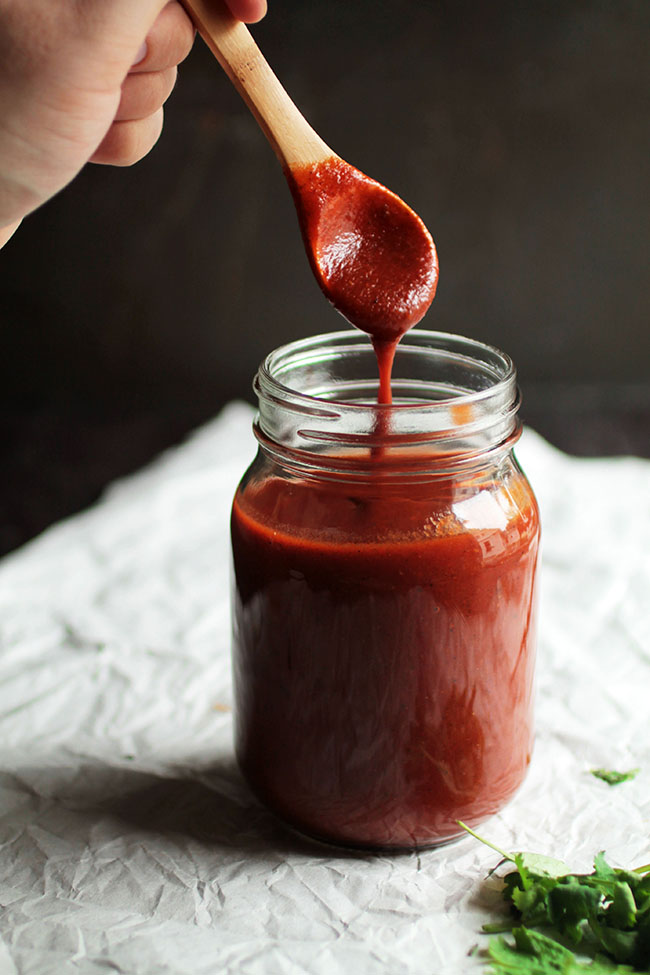 Wooden spoon drizzling enchilada sauce into a mason jar.
