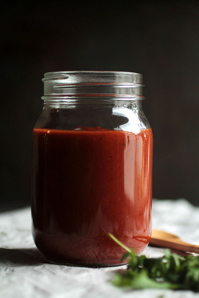 A glass jar filled with dark red enchilada sauce.