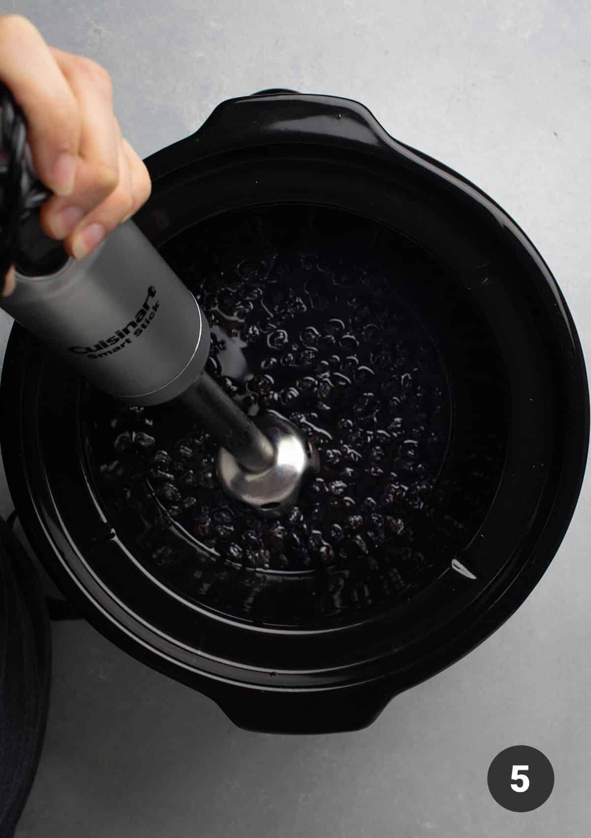 Pulsing cooked blueberries with an immersion blender.
