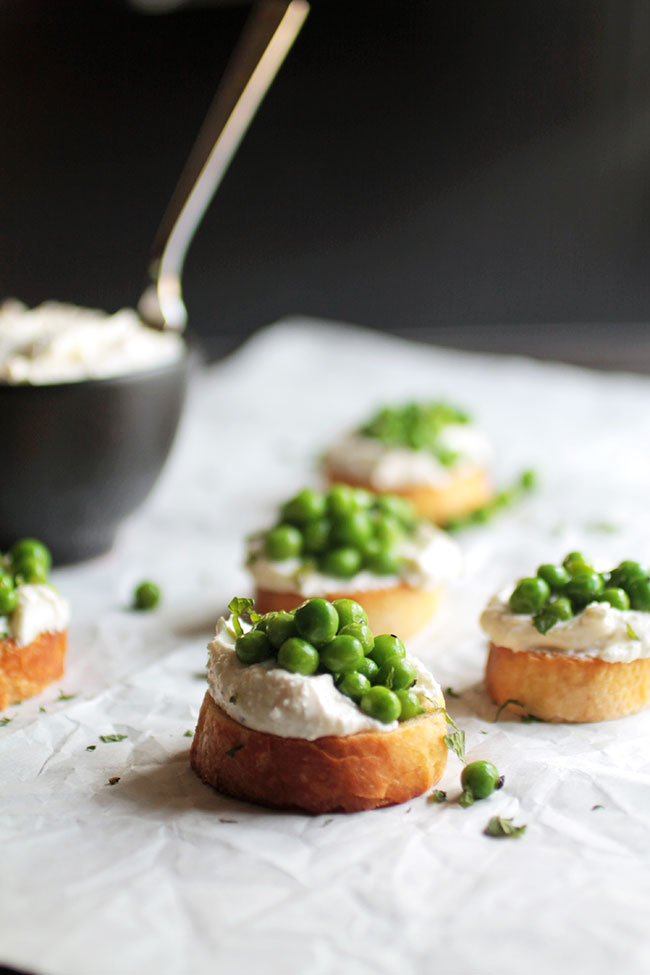 Pea and feta crostini on a dark table lined with white parchment paper.