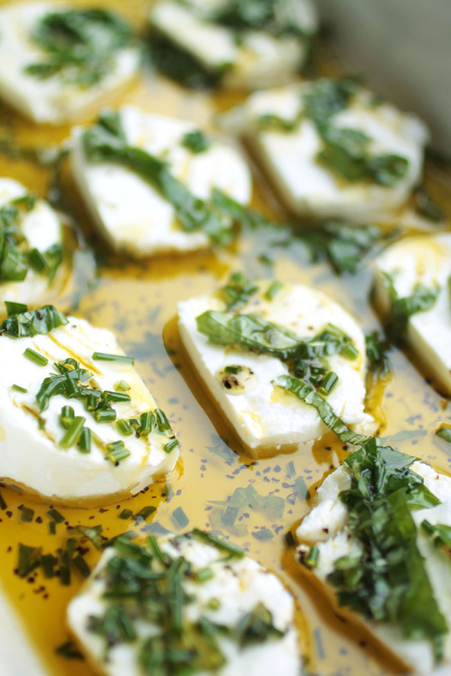 Goat cheese rounds in a dish with olive oil and herbs.