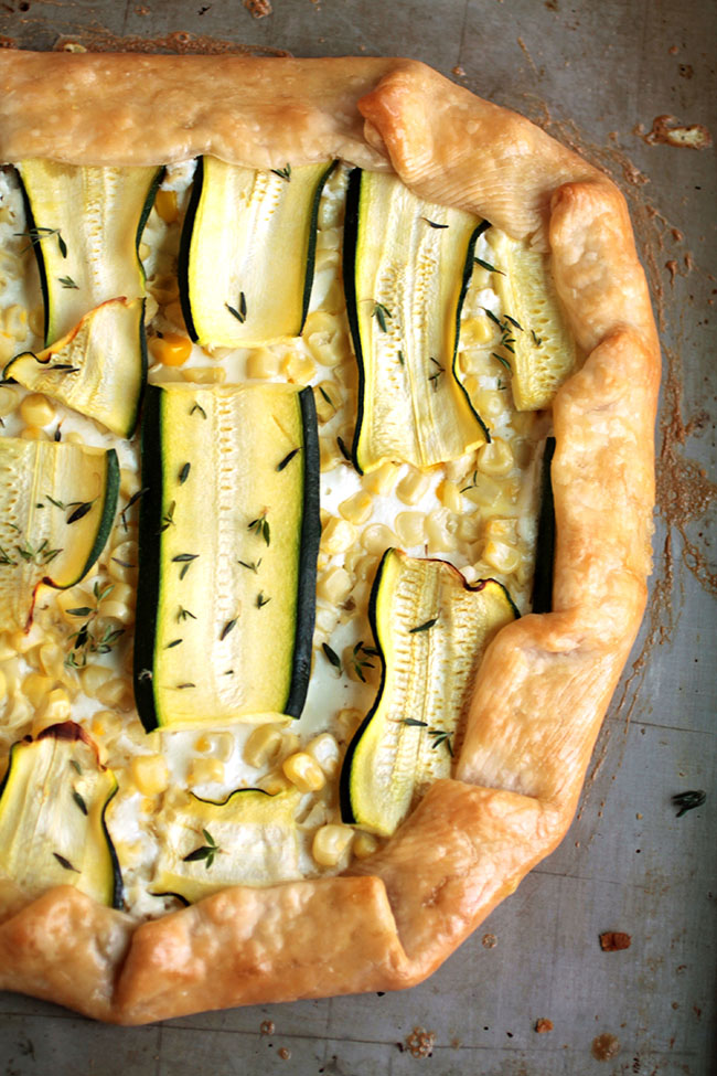 Zucchini galette topped with fresh thyme leaves on a grey baking sheet.