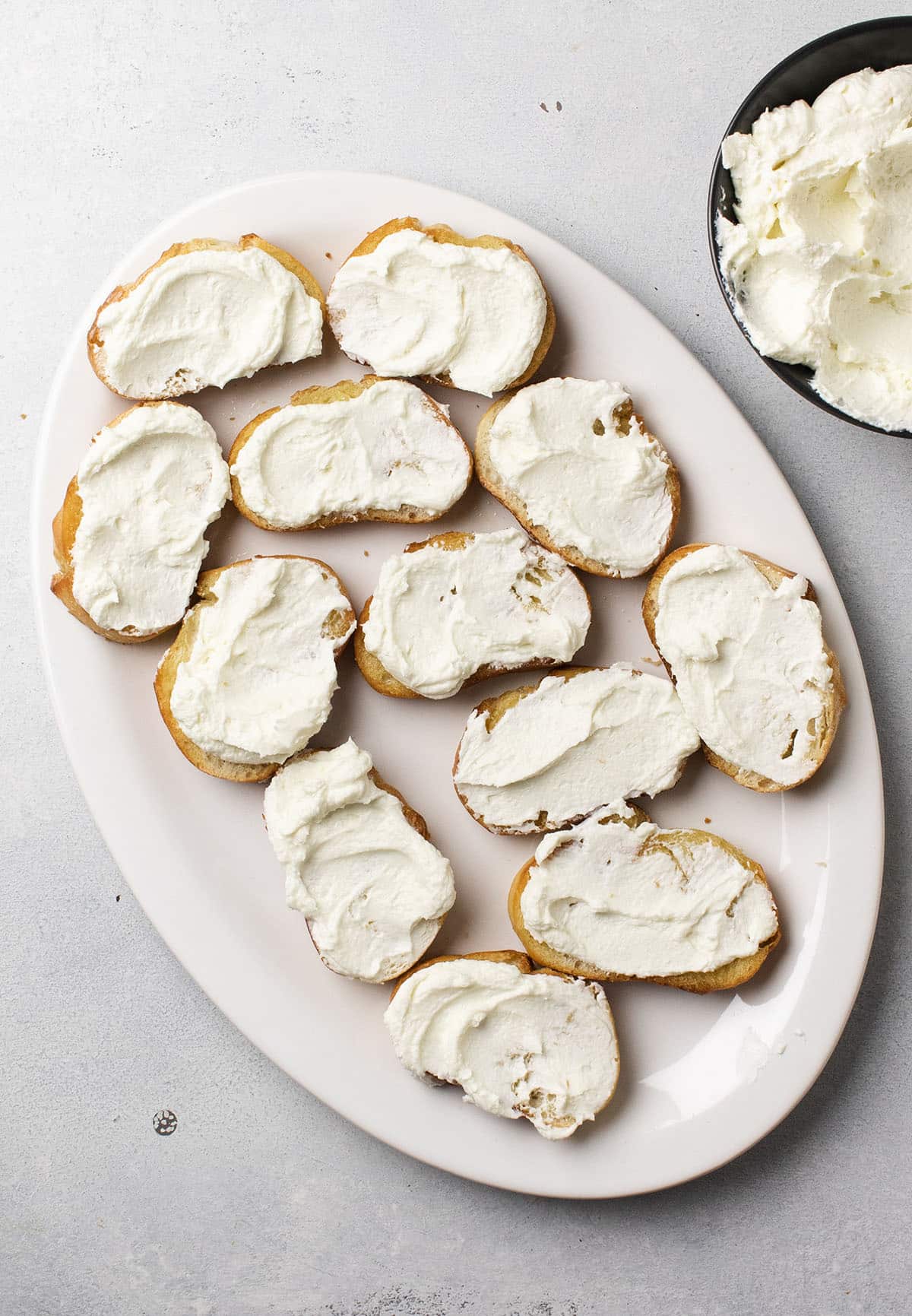 Crostini topped with whipped goat cheese on a white serving platter.
