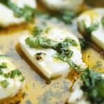 Sliced goat cheese in a white dish with herb marinade.