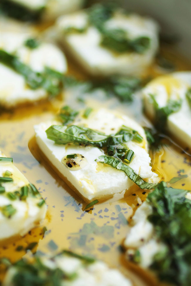 Sliced goat cheese in a baking dish with olive oil and fresh herbs.