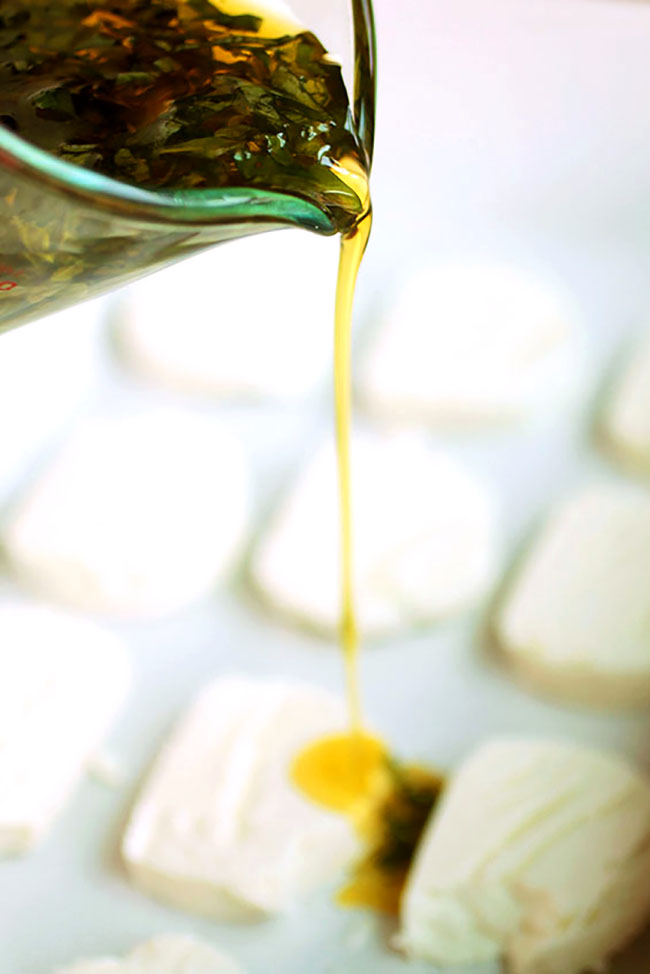 Pouring olive oil over a tray of sliced goat cheese.