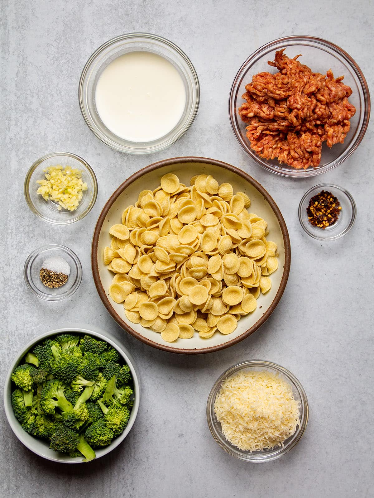 Pasta ingredients organized into individual bowls on a white table.