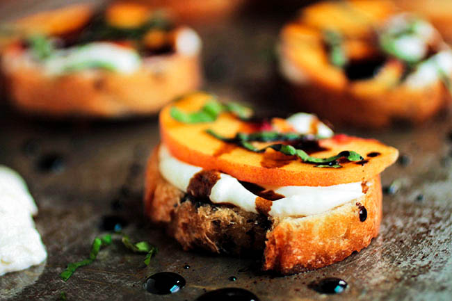 Bruschetta topped with whipped goat cheese, a peach slice, and balsamic vinegar.