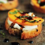 Peach crostini on a dark sheet pan drizzled with balsamic reduction.l