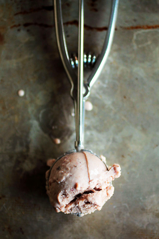 Metal spoon holding a scoop of strawberry ice cream on a metal baking sheet.