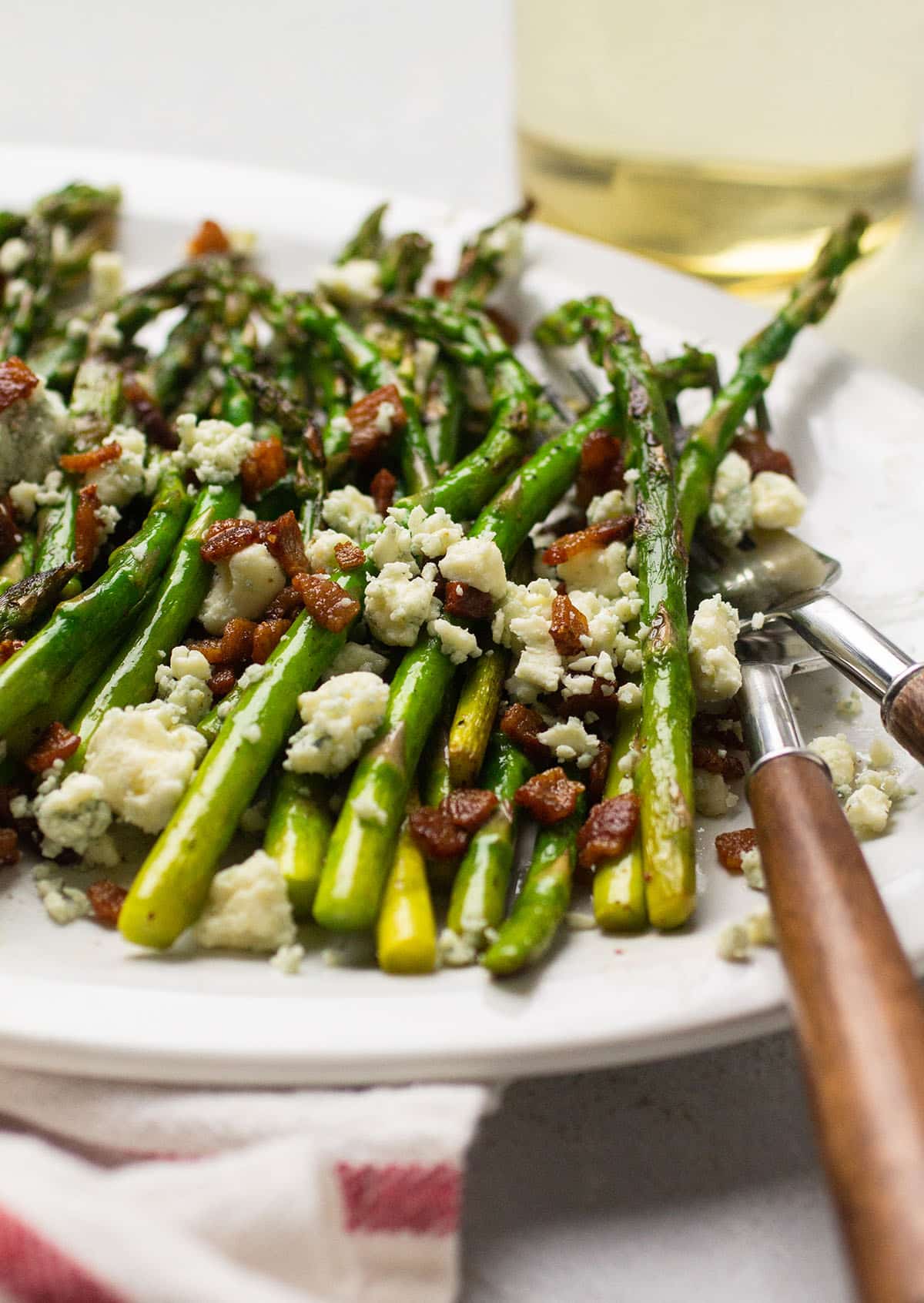 Two wooden forks on a white plate with asparagus, bacon, and blue cheese.