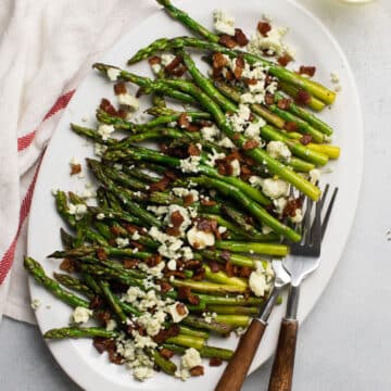 Asparagus with bacon and blue cheese crumbles on a white platter.