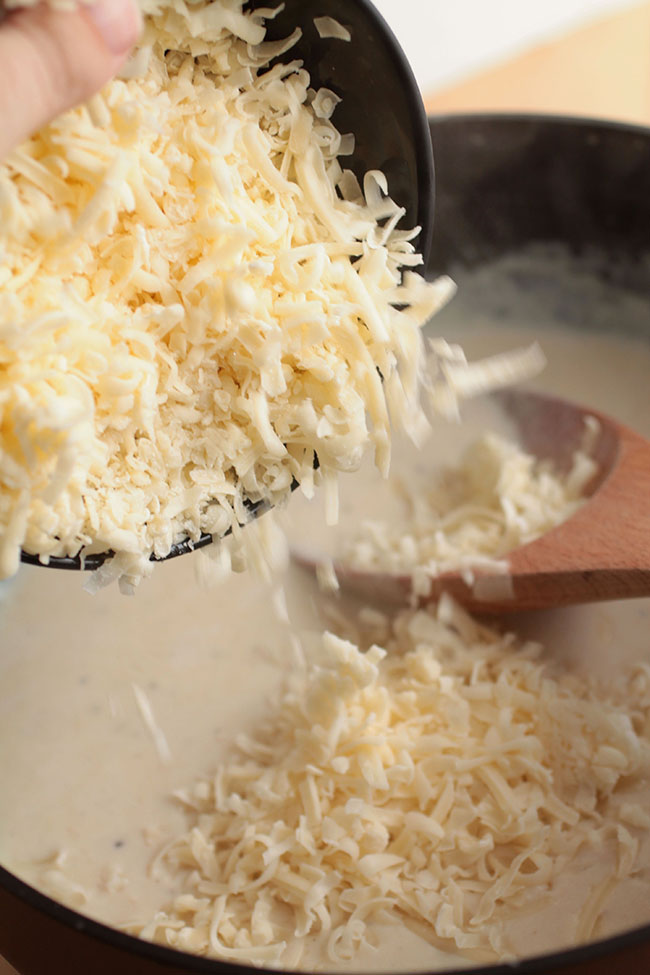 Adding shredded cheese to the sauce.